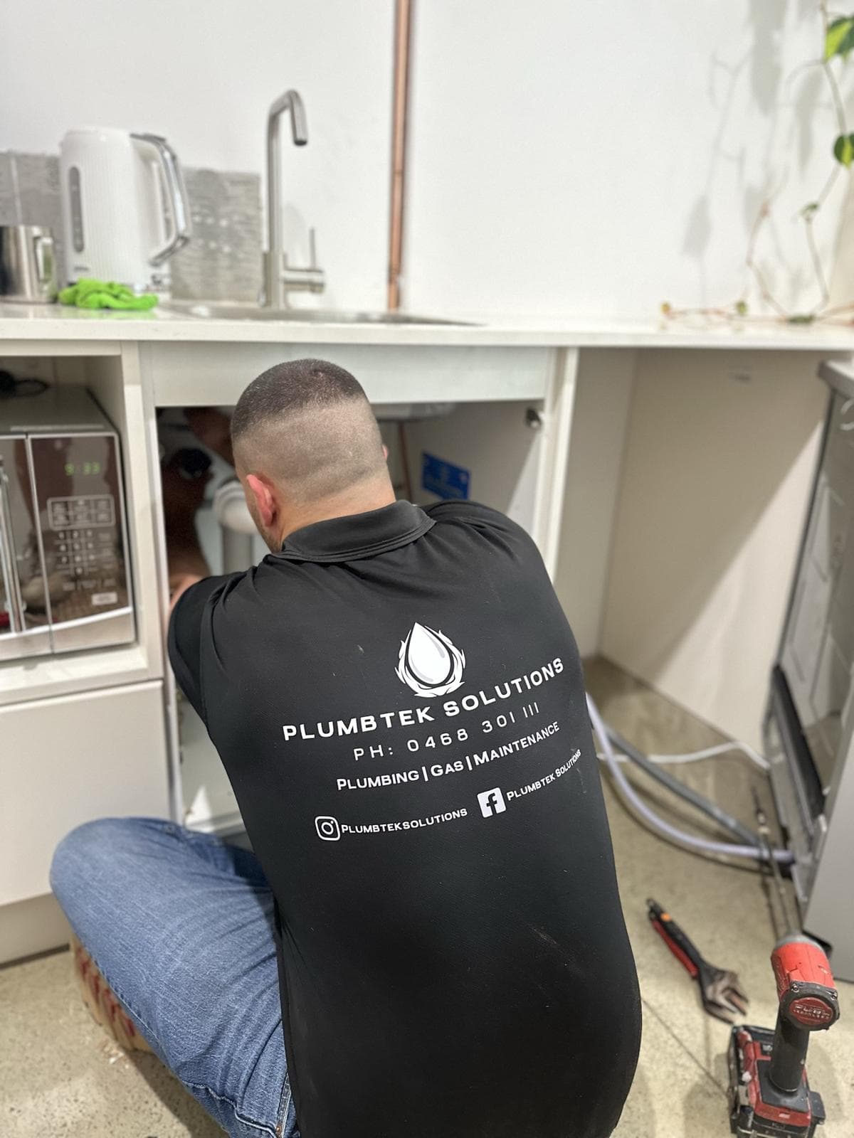A Plumbtek Solutions plumber completing a repair under a kitchen sink